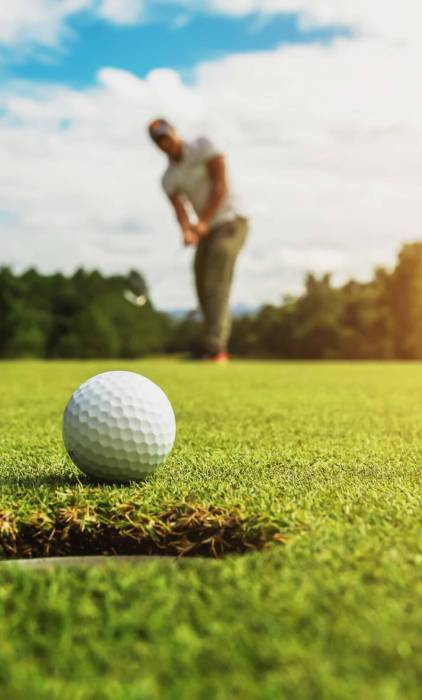 golf player putting golf ball into hole with sunshine